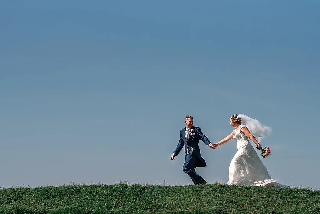 bride and groom running along the top of the hill in Dorset