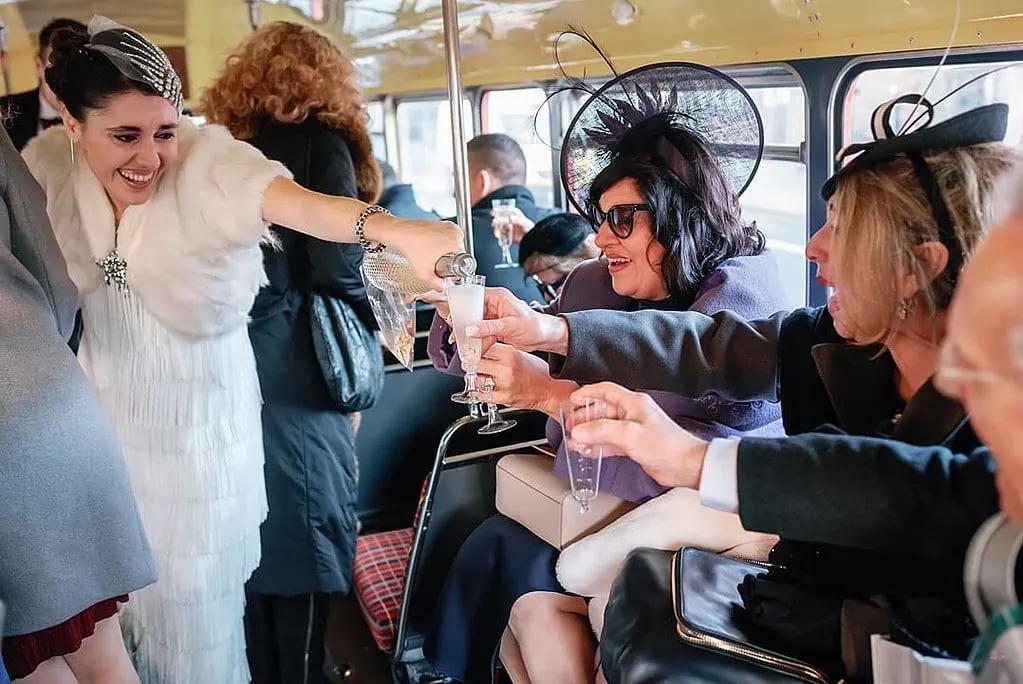 the bride serving champagne to wedding guests on the red London bus
