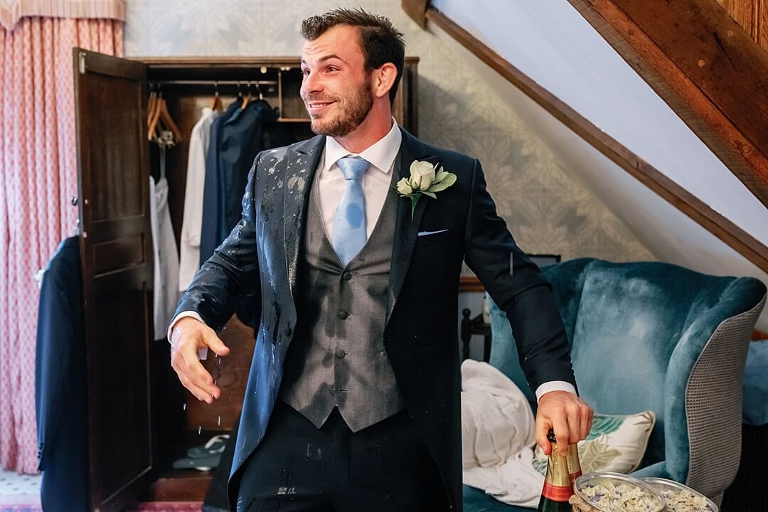 groomsman gets wet opening champagne bottle