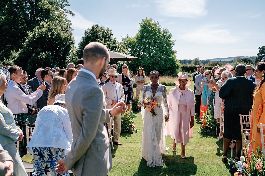 the bride walking down the aisle for the outdoor ceremony at cowdray house