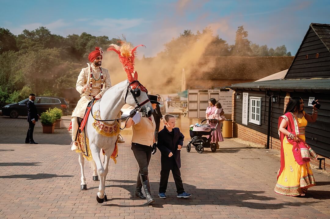 the groom arriving for the indian wedding on a horse at Tewin Bury Farm